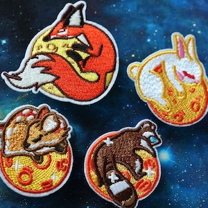 May include: Four embroidered iron-on patches featuring different animals sleeping on a yellow moon. The animals are a fox, a rabbit, a raccoon, and a dog.