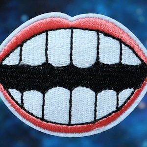 May include: Embroidered patch featuring a cartoon mouth with a wide grin. The patch has white teeth, a black mouth, and red lips, all outlined with a white border. The background is a blurred blue and purple.
