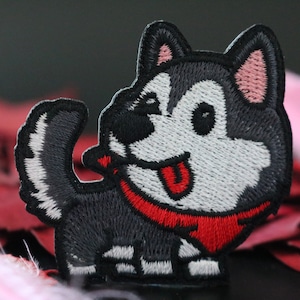 May include: Embroidered patch of a cartoon husky dog with a red bandana. The dog is black, white, and gray with a pink nose and tongue sticking out.