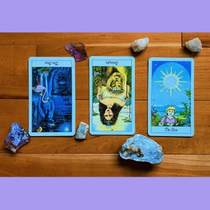 May include: Three tarot cards on a wooden surface. The cards are "The Star", "Strength", and "The Sun".
