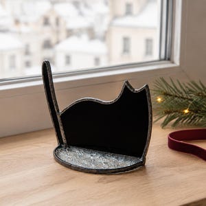 May include: A black stained glass cat silhouette with a raised tail, featuring a textured, clear glass base. The cat figure is outlined in dark metal solder, creating a defined shape that stands upright on a flat surface.