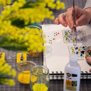 May include: A set of three ceramic mugs with a speckled, cream-colored glaze. Each mug features a different hand-painted design: a blue and green leaf, a yellow flower, and a red berry. The mugs have a simple, modern design.