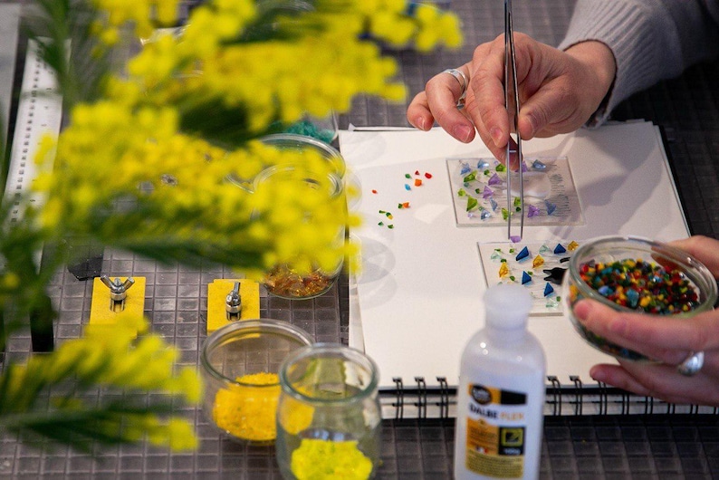 May include: A set of three ceramic mugs with a speckled, cream-colored glaze. Each mug features a different hand-painted design: a blue and green leaf, a yellow flower, and a red berry. The mugs have a simple, modern design.
