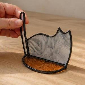 May include: A stained glass cat-shaped stand featuring a white and gray marbled body with a dark metal frame. The base is made of textured amber-colored glass, and the structure includes a vertical tail piece extending upward from the side.