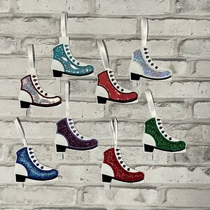 K&ouml;nnte beinhalten: Acht glitzernde Schlittschuh-Anh&auml;nger in verschiedenen Farben, darunter Rot, Blau, Gr&uuml;n und Silber. Jeder Anh&auml;nger hat eine wei&szlig;e Basis und ein wei&szlig;es Band zum Aufh&auml;ngen.