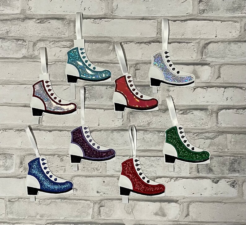 K&ouml;nnte beinhalten: Acht glitzernde Schlittschuh-Anh&auml;nger in verschiedenen Farben, darunter Rot, Blau, Gr&uuml;n und Silber. Jeder Anh&auml;nger hat eine wei&szlig;e Basis und ein wei&szlig;es Band zum Aufh&auml;ngen.