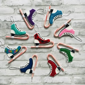 K&ouml;nnte beinhalten: Neun bunte Schlittschuh-Anh&auml;nger, die an Zuckerstangen befestigt sind. Die Anh&auml;nger sind aus Filz und haben Glitzer-Akzente. Die Zuckerstangen sind rot und wei&szlig;.