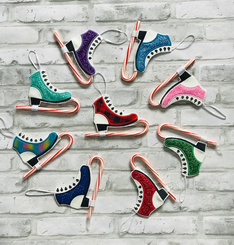 K&ouml;nnte beinhalten: Neun bunte Schlittschuh-Anh&auml;nger, die an Zuckerstangen befestigt sind. Die Anh&auml;nger sind aus Filz und haben Glitzer-Akzente. Die Zuckerstangen sind rot und wei&szlig;.