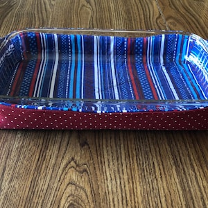 Puede incluir: Un plato para hornear forrado de tela a rayas rojas y azules con ribete de lunares rojos. El plato es de vidrio y tiene dos asas.