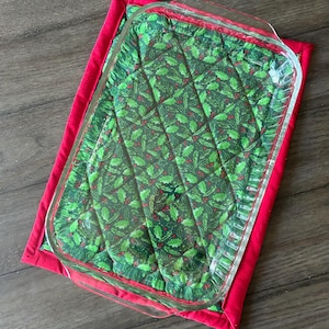 May include: A red and green quilted hot pad with a glass baking dish on top. The hot pad has a holly pattern.