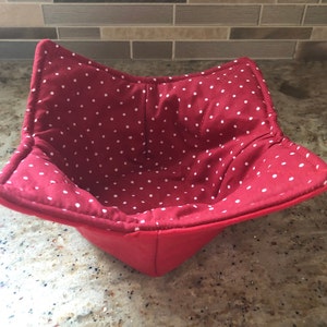 May include: Red fabric bowl with white polka dots. The bowl is quilted and has a square shape.
