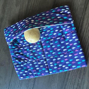May include: A blue fabric pouch with a white trim and a pattern of small teal, pink, and white raindrops. A light brown ball is inside the pouch.