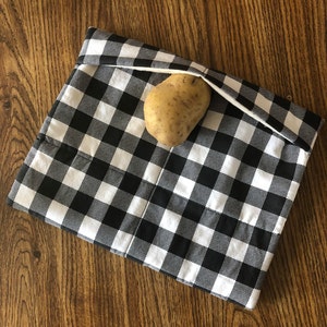 May include: A black and white gingham fabric pouch with a single potato inside. The pouch is folded over at the top and has a small loop at the top.