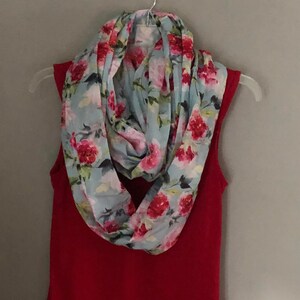 May include: A light blue floral infinity scarf with a pink and red floral pattern.