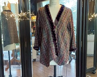 May include: A multi-colored tweed jacket with a velvet trim and a ruffled collar. The jacket is displayed on a mannequin in front of a mirrored screen.