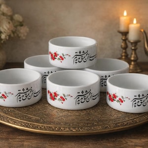 May include: Six white ceramic bowls with a floral design and script are arranged on a decorative gold tray. The bowls are cylindrical and have a red floral pattern with script. The tray is ornate and sits on a wooden surface.