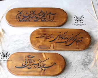 May include: Three wooden oval signs with calligraphy in black ink. The signs are made of light brown wood and have a natural finish. The calligraphy is in Arabic script and is a beautiful example of traditional Islamic art.