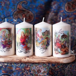 May include: Four white pillar candles with colorful images and calligraphy printed on them. The candles are arranged in a row on a wooden surface.