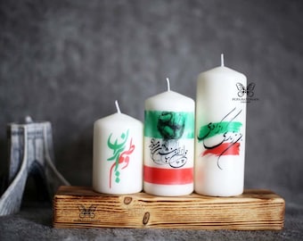 May include: Three white pillar candles with green, red, and white designs. The candles are on a wooden stand with a butterfly logo. The candles feature Persian calligraphy and a fist.