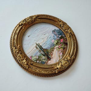 May include: A round oil painting featuring a textured landscape with thick impasto brushstrokes in shades of blue, pink, and green, encased in an ornate, circular gold frame with intricate relief carvings along the outer edge.