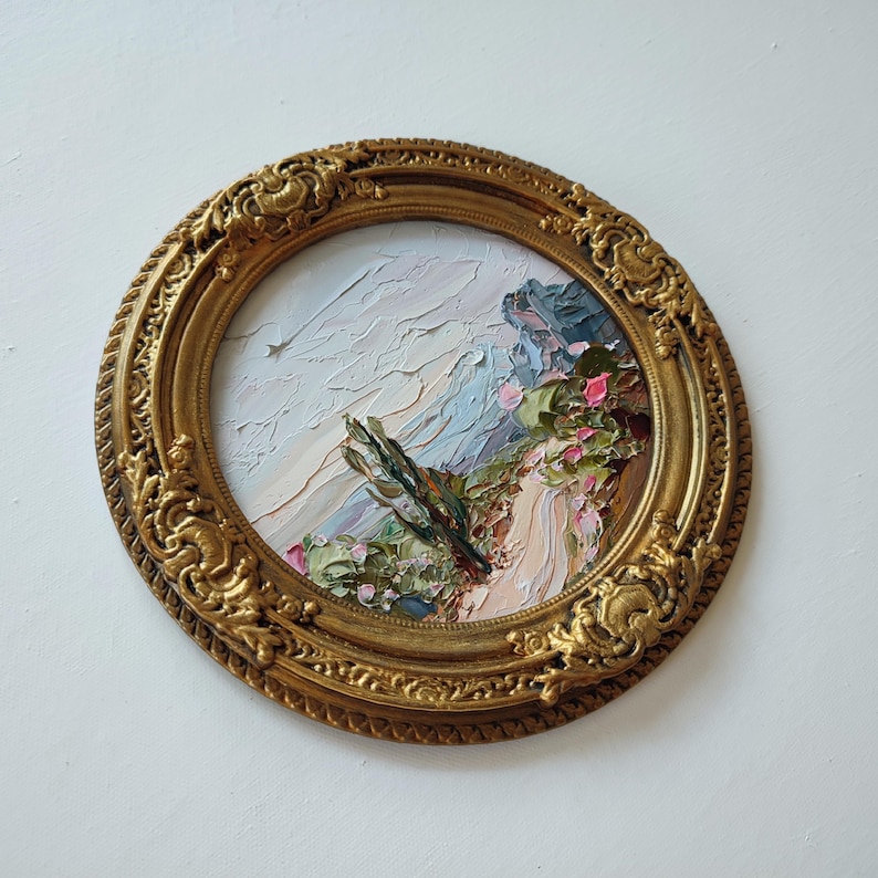 May include: A round oil painting featuring a textured landscape with thick impasto brushstrokes in shades of blue, pink, and green, encased in an ornate, circular gold frame with intricate relief carvings along the outer edge.