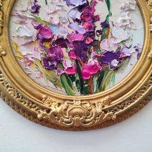 May include: An oil painting featuring a thick impasto floral arrangement with vibrant shades of purple, magenta, pink, and white petals against green stems. The artwork is encased in a circular, ornate, metallic gold frame with detailed relief.