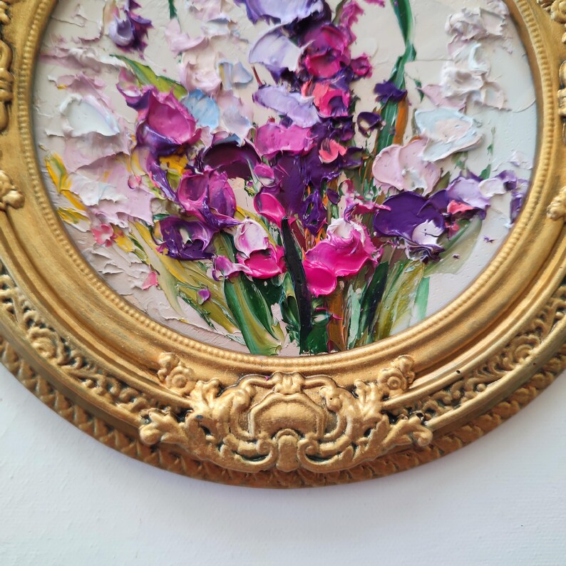 May include: An oil painting featuring a thick impasto floral arrangement with vibrant shades of purple, magenta, pink, and white petals against green stems. The artwork is encased in a circular, ornate, metallic gold frame with detailed relief.