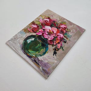 Puede incluir: Pintura al &oacute;leo de un ramo de flores rosas y rojas en un jarr&oacute;n verde. La obra presenta pinceladas gruesas y un aspecto texturizado. El jarr&oacute;n es redondo y se apoya sobre una superficie lila claro.
