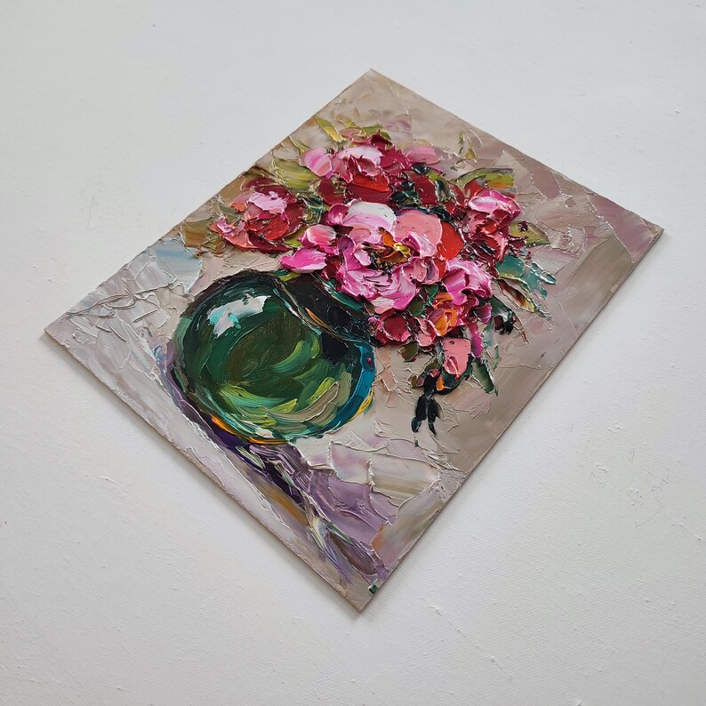 Puede incluir: Pintura al &oacute;leo de un ramo de flores rosas y rojas en un jarr&oacute;n verde. La obra presenta pinceladas gruesas y un aspecto texturizado. El jarr&oacute;n es redondo y se apoya sobre una superficie lila claro.