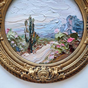 May include: An oval oil painting featuring a desert landscape with a tall cactus, rocky formations, and a winding path, rendered with thick impasto brushstrokes in shades of blue, green, and pink, enclosed in an ornate, antique gold-toned frame.