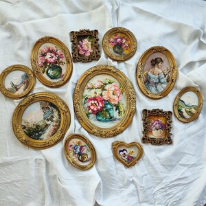 May include: A collection of ten assorted wall art pieces in ornate gold frames, featuring oil paintings of floral bouquets, landscapes, and a portrait, displayed in various shapes including oval, rectangular, and heart-shaped designs.