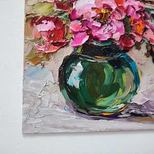Puede incluir: Pintura al &oacute;leo de un ramo de flores rosas y rojas en un jarr&oacute;n verde oscuro. El jarr&oacute;n redondo descansa sobre una superficie blanca. La pintura utiliza una t&eacute;cnica de empaste, con pinceladas visibles.