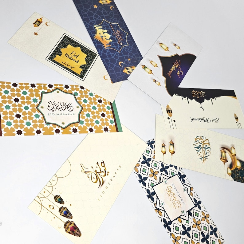May include: Assortment of Eid Mubarak greeting cards with gold and blue accents. The cards feature intricate patterns, calligraphy, and lanterns. The text on the cards reads "Eid Mubarak" in Arabic and English.