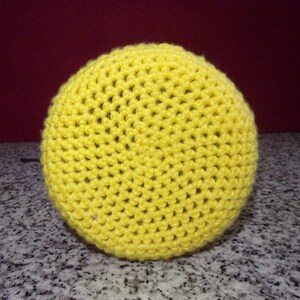 May include: A bright yellow crocheted round cushion or pouf. The cushion is made with a simple stitch pattern and has a smooth, even texture.