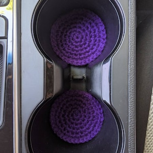 May include: Two purple crocheted cup holders in a car's cup holder.