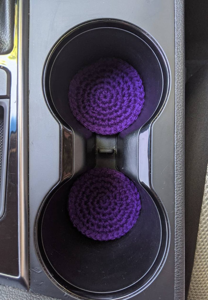 May include: Two purple crocheted cup holders in a car's cup holder.
