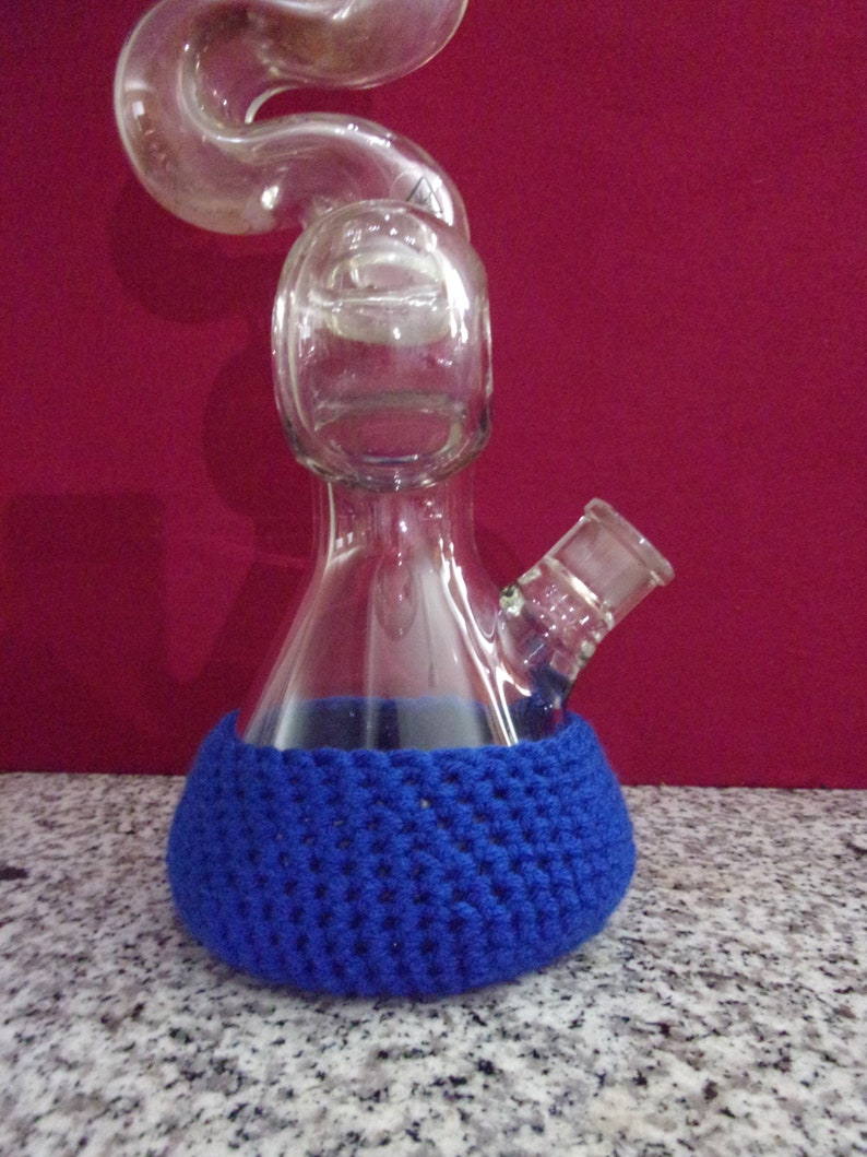 May include: A clear glass beaker with a curved neck and a blue crocheted cover. The beaker has a small spout on the side.