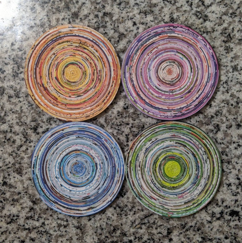 May include: Four round coasters made of recycled paper with different colorful patterns. The coasters are layered with different colors of paper, creating a unique and eye-catching design.