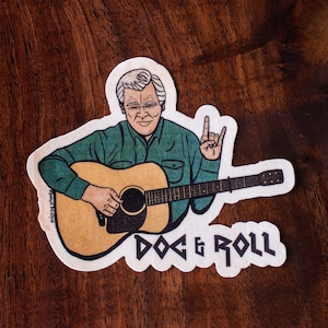 May include: A sticker featuring a cartoon illustration of a man playing an acoustic guitar, with the text "DOC & ROLL". The man is wearing a green shirt and giving a rock and roll hand gesture.