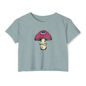 May include: A light blue t-shirt with a graphic of a pink mushroom with a single eye on the cap.