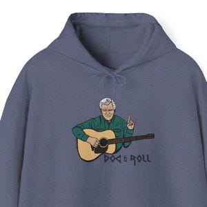 May include: A blue hooded sweatshirt featuring a cartoon illustration of a man playing a guitar. The text "Doc & Roll" is printed below the image.