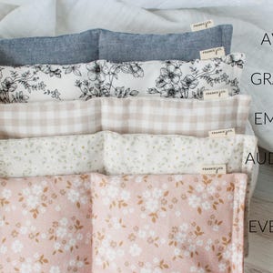 May include: A stack of five fabric items with different floral and patterned designs. The top item is a solid blue-gray, followed by a black and white floral print, a tan gingham, a white floral print, and a pink floral print. Each item has a small tag that says "frankie & co.".