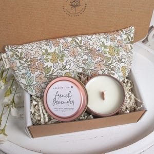 Puede incluir: Una caja de regalo que contiene una m&aacute;scara para los ojos con estampado floral, una vela de lata de oro rosa con una mecha de madera y una vela con el texto "French Lavender". La caja est&aacute; llena de relleno de papel.