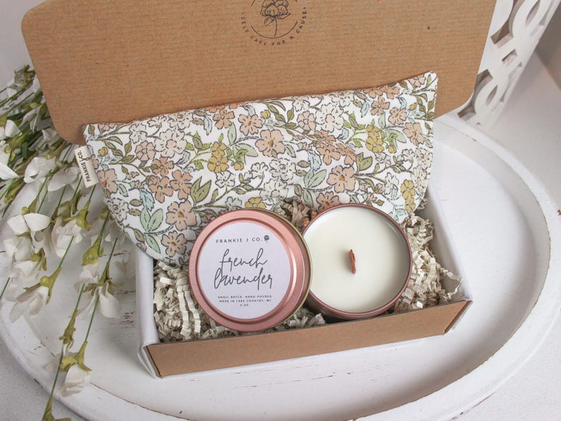 Puede incluir: Una caja de regalo que contiene una m&aacute;scara para los ojos con estampado floral, una vela de lata de oro rosa con una mecha de madera y una vela con el texto "French Lavender". La caja est&aacute; llena de relleno de papel.