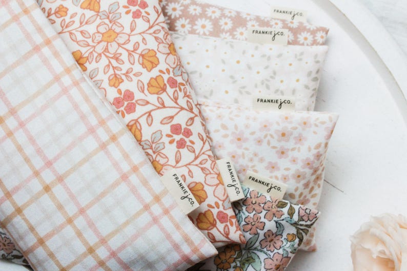 May include: Close-up of several fabric pieces with floral and plaid patterns. The fabrics feature a variety of colors, including peach, pink, and white. Each piece has a tag that reads "FRANKIE jco."