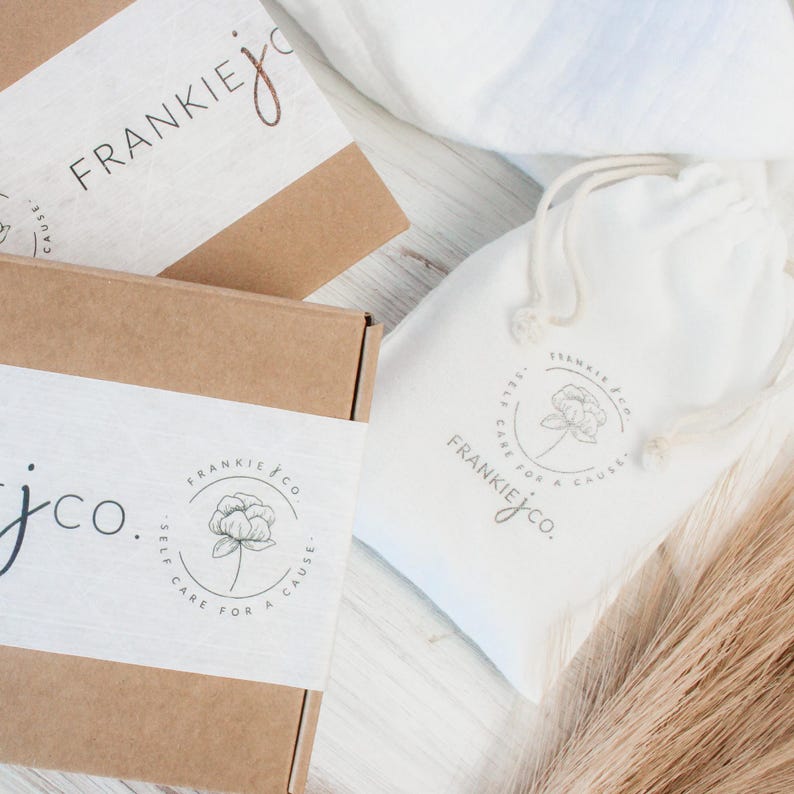 K&ouml;nnte beinhalten: Zwei braune Pappkartons mit wei&szlig;en Etiketten. Die Etiketten zeigen ein Blumenmuster und den Text "Frankie jco. Self care for a cause". Im Hintergrund befindet sich ein wei&szlig;er Kordelbeutel mit einem &auml;hnlichen Blumenmuster und dem Text "Frankie jco. Self care for a cause".