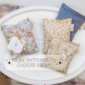 May include: An assortment of small, square fabric sachets in various floral and solid patterns. One sachet is tied with twine and a tag. The sachets are in shades of blue, beige, and floral prints. Text on the image reads "MORE PATTERNS TO CHOOSE FROM!"