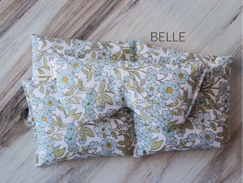 May include: A folded eye mask featuring a floral pattern with light blue and yellow flowers on a white background. The word "BELLE" is printed on the mask. The tag reads "FRANKIE JESS".