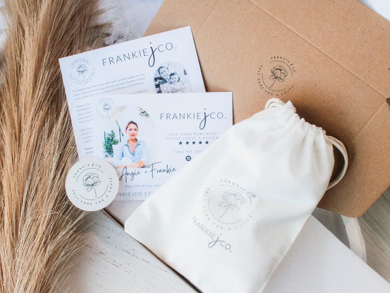 May include: An overhead shot of a product package with branding. The package includes a white drawstring bag, a round sticker, and two cards with the text "FRANKIEJCO." and a floral logo. A brown cardboard box is also visible.