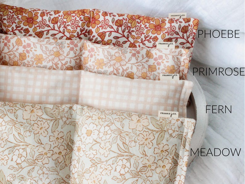 May include: Four fabric-covered pillows with floral and gingham patterns in shades of orange, pink, and beige. The pillows are labeled "Phoebe", "Primrose", "Fern", and "Meadow". Each pillow has a small tag that says "frankie jco."